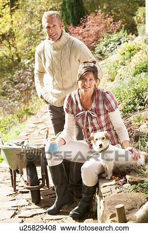 Couple With Dog Having Coffee Break Whilst Working Outdoors In Garden View Large Photo Image Stock Photo - Couple With Dog Having Coffee Break Whilst Working Outdoors In Garden. Fotosearch