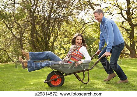 Stock Image - Couple With Man Giving Woman Ride In Wheelbarrow. Fotosearch