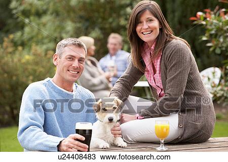 Stock Image - Couple With Pet Dog Outdoors Enjoying Drink In Pub Garden. Fotosearch