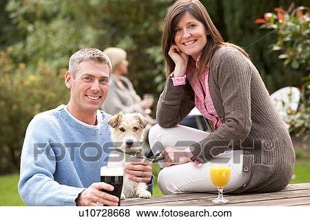 Couple With Pet Dog Outdoors Enjoying Drink In Pub Garden View Large Photo Image Stock Photo - Couple With Pet Dog Outdoors Enjoying Drink In Pub Garden. Fotosearch