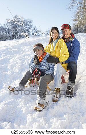 Stock Image - Family Enjoying Sledging Down Snowy Hill. Fotosearch