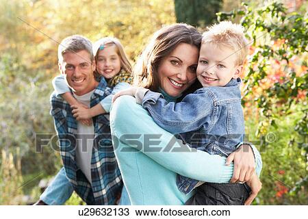 Stock Image - Family Group Outdoors In Autumn Landscape With Parents Giving Chiildren Piggyback. Fotosearch