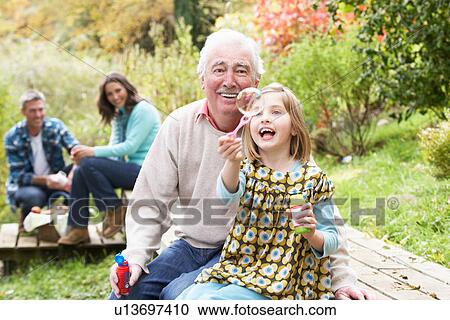 Stock Image - Grandfather And Granddaughter Blowing Bubbles On Family Picnic. Fotosearch