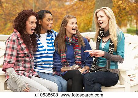 Stock Photo - Group Of Four Teenage Girls Sitting On Bench In Autumn Park. Fotosearch