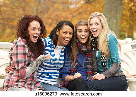 Stock Photo - Group Of Four Teenage Girls Sitting On Bench In Autumn Park. Fotosearch