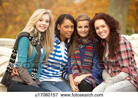 Stock Photo - Group Of Four Teenage Girls Sitting On Bench In Autumn Park. Fotosearch