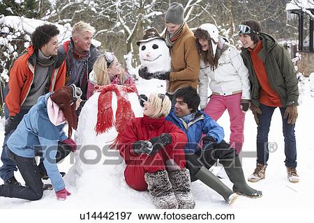 Stock Photo - Group Of Teenage Friends Building Snowman In Garden. Fotosearch