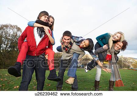 Stock Image - Group Of Teenage Friends Having Piggyback Rides In Autumn Landscape. Fotosearch