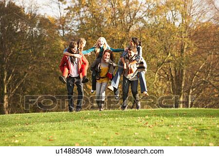 Stock Photo - Group Of Teenage Friends Having Piggyback Rides In Autumn Landscape. Fotosearch
