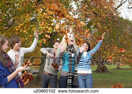 Stock Image - Group Of Teenage Friends Throwing Leaves In Autumn Landscape. Fotosearch