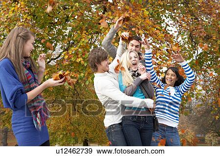 Stock Photo - Group Of Teenage Friends Throwing Leaves In Autumn Landscape. Fotosearch