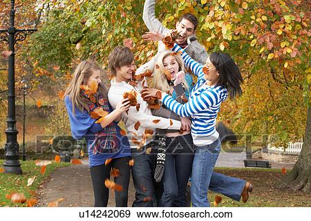Stock Photo - Group Of Teenage Friends Throwing Leaves In Autumn Landscape. Fotosearch