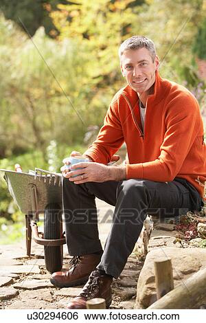 Stock Photograph - Man Having Coffee Break Whilst Working Outdoors In Garden. Fotosearch