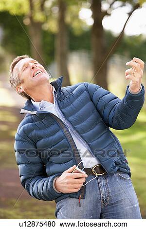 Stock Image - Man Listening To MP3 Whilst Walking In Autumn Park. Fotosearch