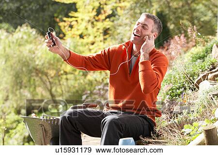 Man Outdoors Listening To MP3 Player Whilst On Break From Gardening View Large Photo Image Stock Photo - Man Outdoors Listening To MP3 Player Whilst On Break From Gardening. Fotosearch