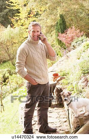 Man Outdoors On Mobile Phone With Dog Whilst On Break From Gardening View Large Photo Image Picture - Man Outdoors On Mobile Phone With Dog Whilst On Break From Gardening. Fotosearch