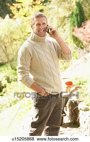 Stock Photo - Man Outdoors On Mobile Phone With Dog Whilst On Break From Gardening. Fotosearch