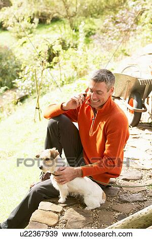 Man Outdoors On Mobile Phone With Dog Whilst On Break From Gardening View Large Photo Image Stock Photo - Man Outdoors On Mobile Phone With Dog Whilst On Break From Gardening. Fotosearch