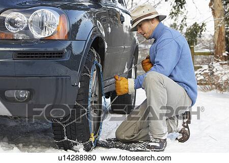 Stock Image - Man Putting Snow Chains Onto Tyre Of Car. Fotosearch