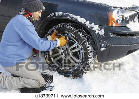 Stock Image - Man Putting Snow Chains Onto Tyre Of Car. Fotosearch