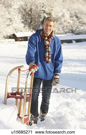 Stock Image - Middle Aged Man Standing In Snowy Landscape Holding Sledge. Fotosearch