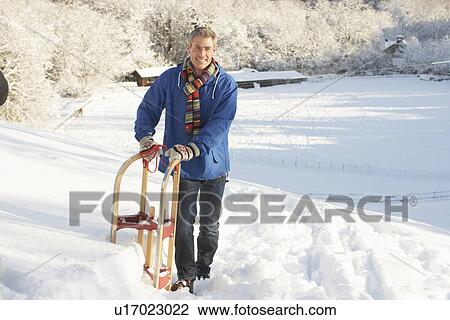 Stock Image - Middle Aged Man Standing In Snowy Landscape Holding Sledge. Fotosearch