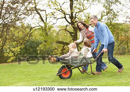 Stock Image - Parents Giving Children Ride In Wheelbarrow. Fotosearch