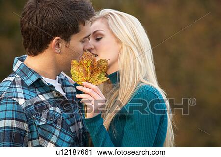 Stock Image - Romantic Teenage Couple Kissing Behind Autumn Leaf. Fotosearch