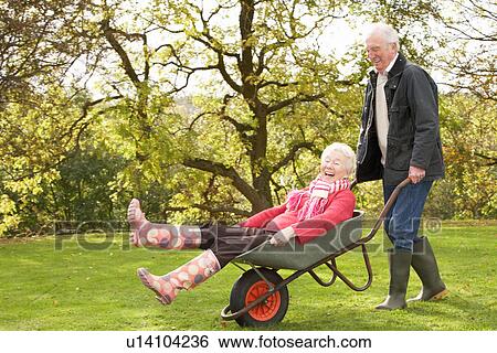 Stock Photograph - Senior Couple Man Giving Woman Ride In Wheelbarrow. Fotosearch