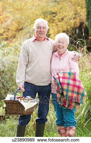 Stock Photo - Senior Couple Outdoors With Picnic Basket By Autumn Woodland. Fotosearch