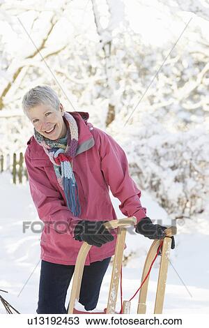 Stock Image - Senior Woman Holding Sledge In Snowy Landscape. Fotosearch