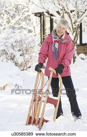Stock Photo - Senior Woman Holding Sledge In Snowy Landscape. Fotosearch