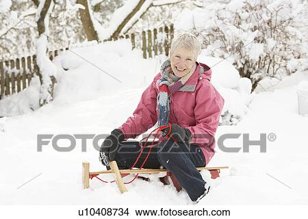 Picture - Senior Woman Sitting On Sledge In Snowy Landscape. Fotosearch