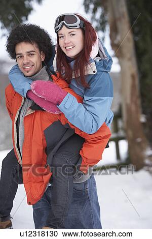 Stock Image - Teenage Boy Giving Girl Piggyback In Snowy Landscape. Fotosearch