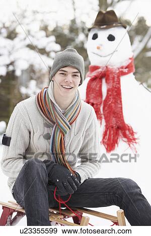 Stock Photo - Teenage Boy With Sledge Next To Snowman. Fotosearch