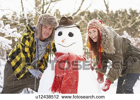 Stock Image - Teenage Couple Building Snowman. Fotosearch