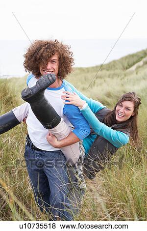 Stock Photo - Teenage Couple Having Piggy Back Ride In Sand Dunes. Fotosearch