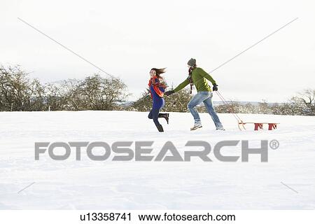 Stock Image - Teenage Couple Pulling Sledge Across Snowy Field. Fotosearch