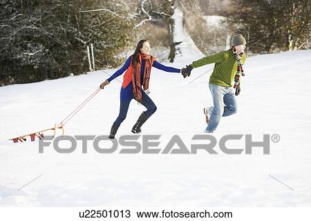 Stock Image - Teenage Couple Pulling Sledge Across Snowy Field. Fotosearch