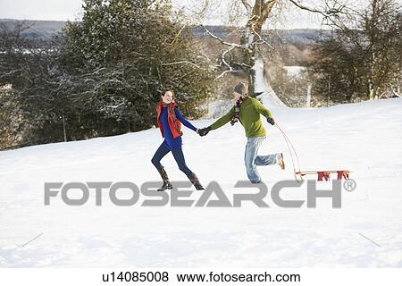 Stock Photo - Teenage Couple Pulling Sledge Across Snowy Field. Fotosearch
