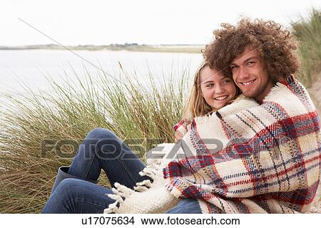 Picture - Teenage Couple Sitting In Sand Dunes Wrapped In Blanket. Fotosearch