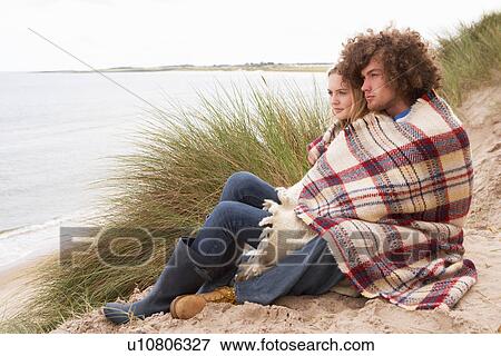 Stock Photo - Teenage Couple Sitting In Sand Dunes Wrapped In Blanket. Fotosearch