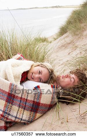 Stock Photo - Teenage Couple Sitting In Sand Dunes Wrapped In Blanket. Fotosearch