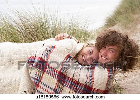 Stock Photograph - Teenage Couple Sitting In Sand Dunes Wrapped In Blanket. Fotosearch