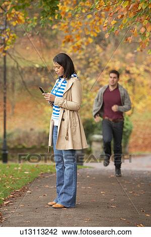 Teenage Girl Making Mobile Phone Call With Boyfriend Running Towards Her In Background View Large Photo Image Stock Image - Teenage Girl Making Mobile Phone Call With Boyfriend Running Towards Her In Background. Fotosearch