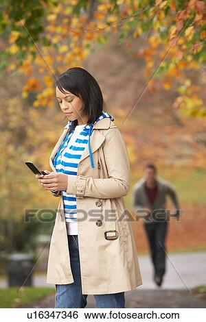 Teenage Girl Making Mobile Phone Call With Boyfriend Running Towards Her In Background View Large Photo Image Stock Photograph - Teenage Girl Making Mobile Phone Call With Boyfriend Running Towards Her In Background. Fotosearch