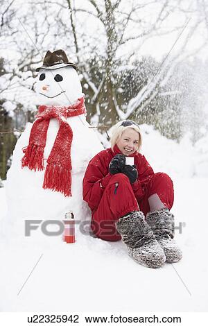 Stock Image - Teenage Girl Next To Snowman With Flask And Hot Drink. Fotosearch