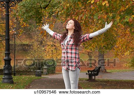 Stock Photograph - Teenage Girl Standing In Autumn Park With Arms Outstretched. Fotosearch