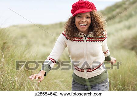 Stock Image - Teenage Girl Walking Through Sand Dunes Wearing Warm Clothing. Fotosearch