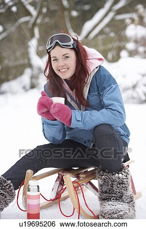 Stock Photograph - Teenage Girl With Sledge Next To Snowman With Flask And Hot Drink. Fotosearch